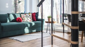 A modern living room with a green sofa, a wooden staircase, and large windows offering a view of trees. - Stare Sady Kopytówka (Brzeznica)