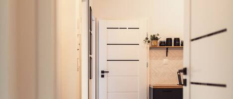 A hallway leading to a kitchen with a white door, wooden flooring, and a dining area with chairs.