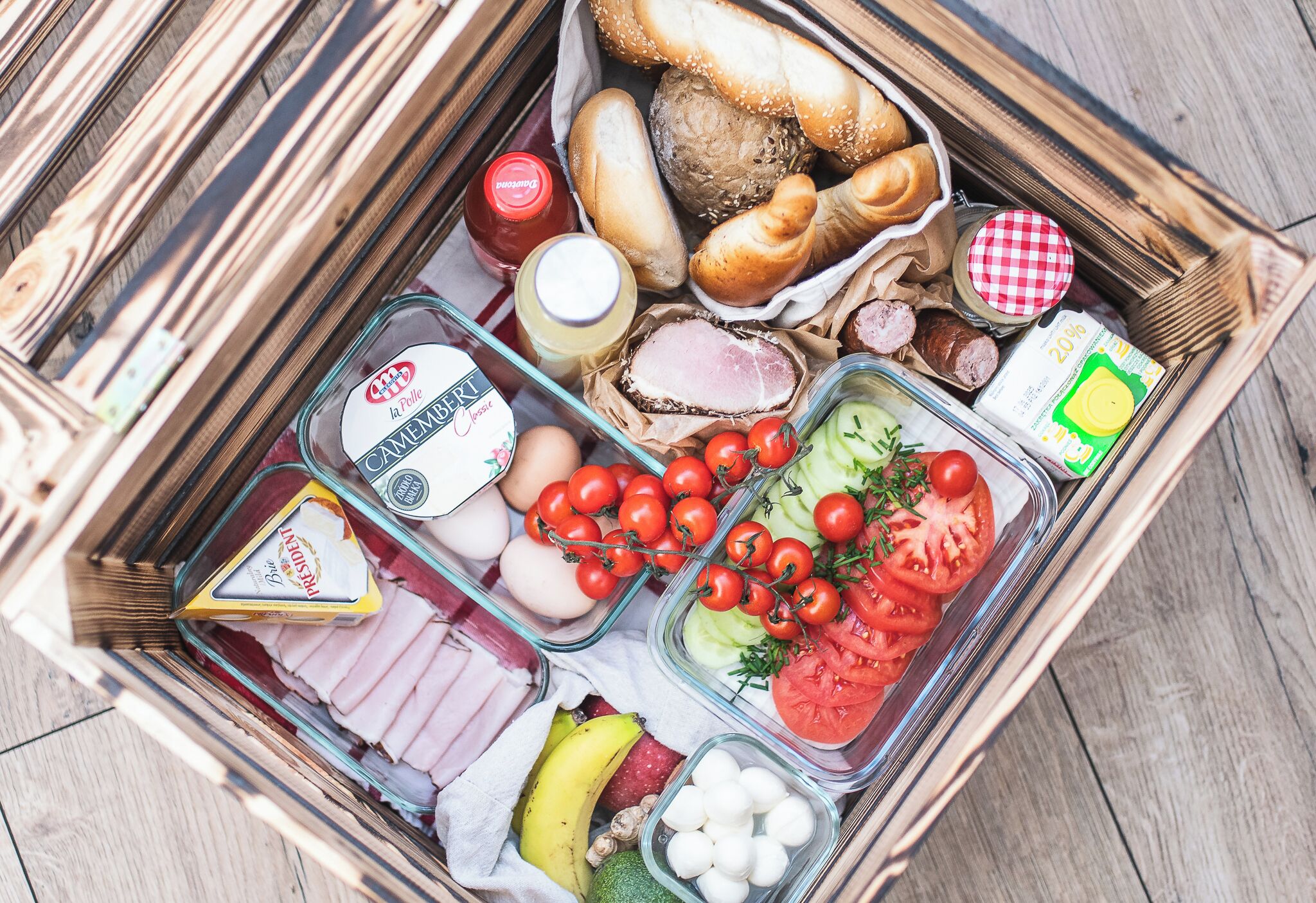 Una caja de madera llena de diversos alimentos, como pan, queso, tomates, pepinos y carne.