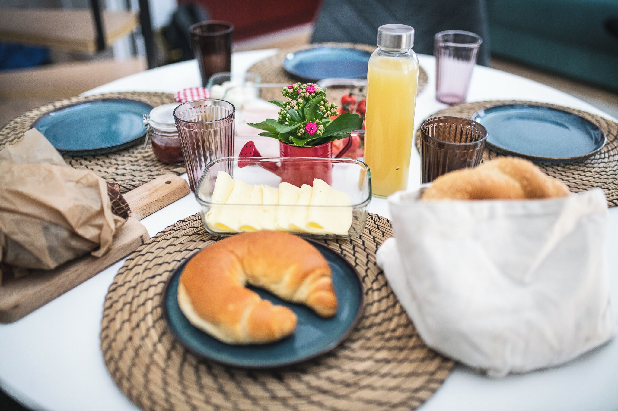 A breakfast setting with croissants, cheese, and juice on a woven placemat.