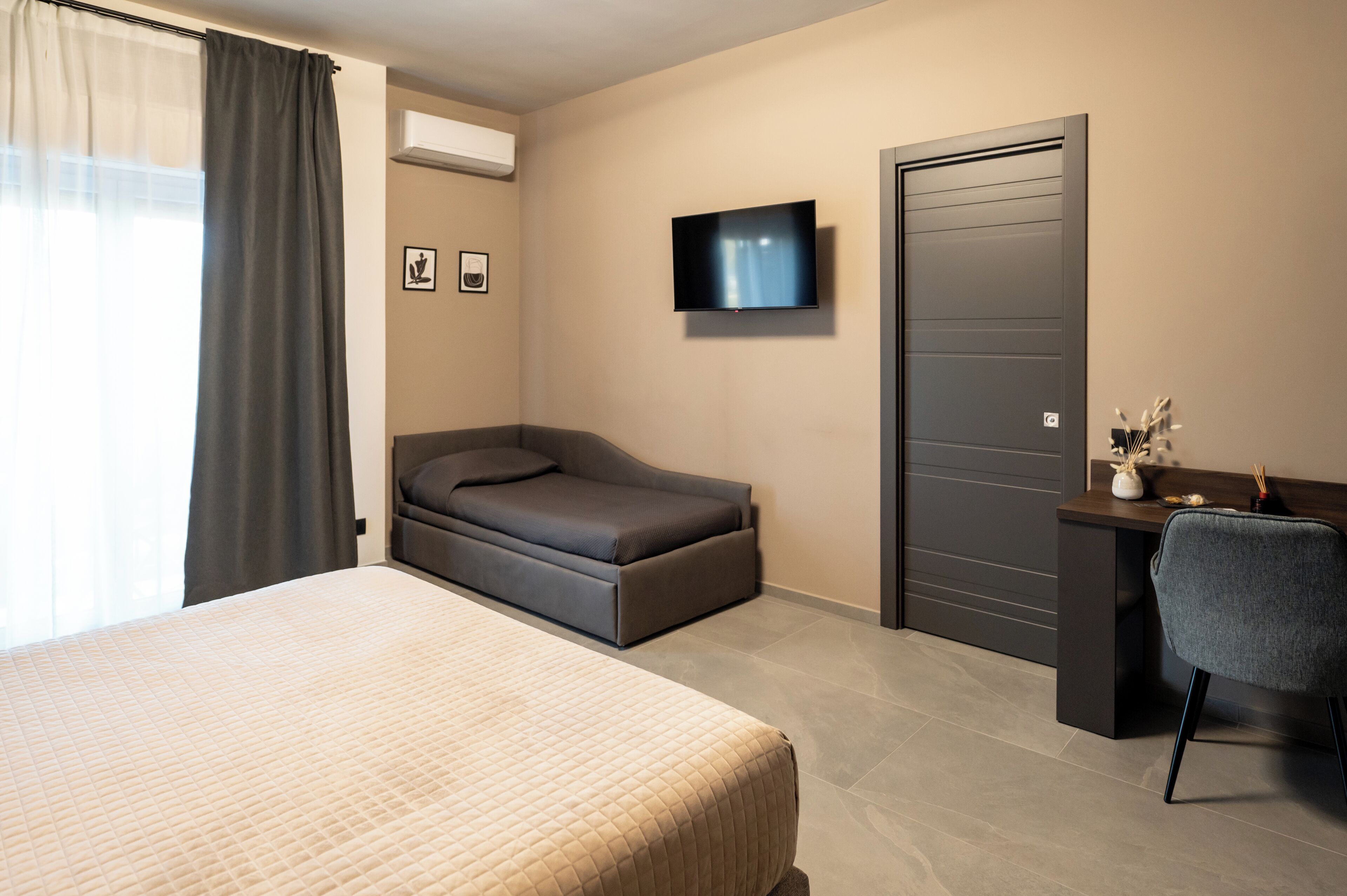Una camera d'hotel con un letto, un divano letto, una scrivania con una sedia, una televisione e una porta.