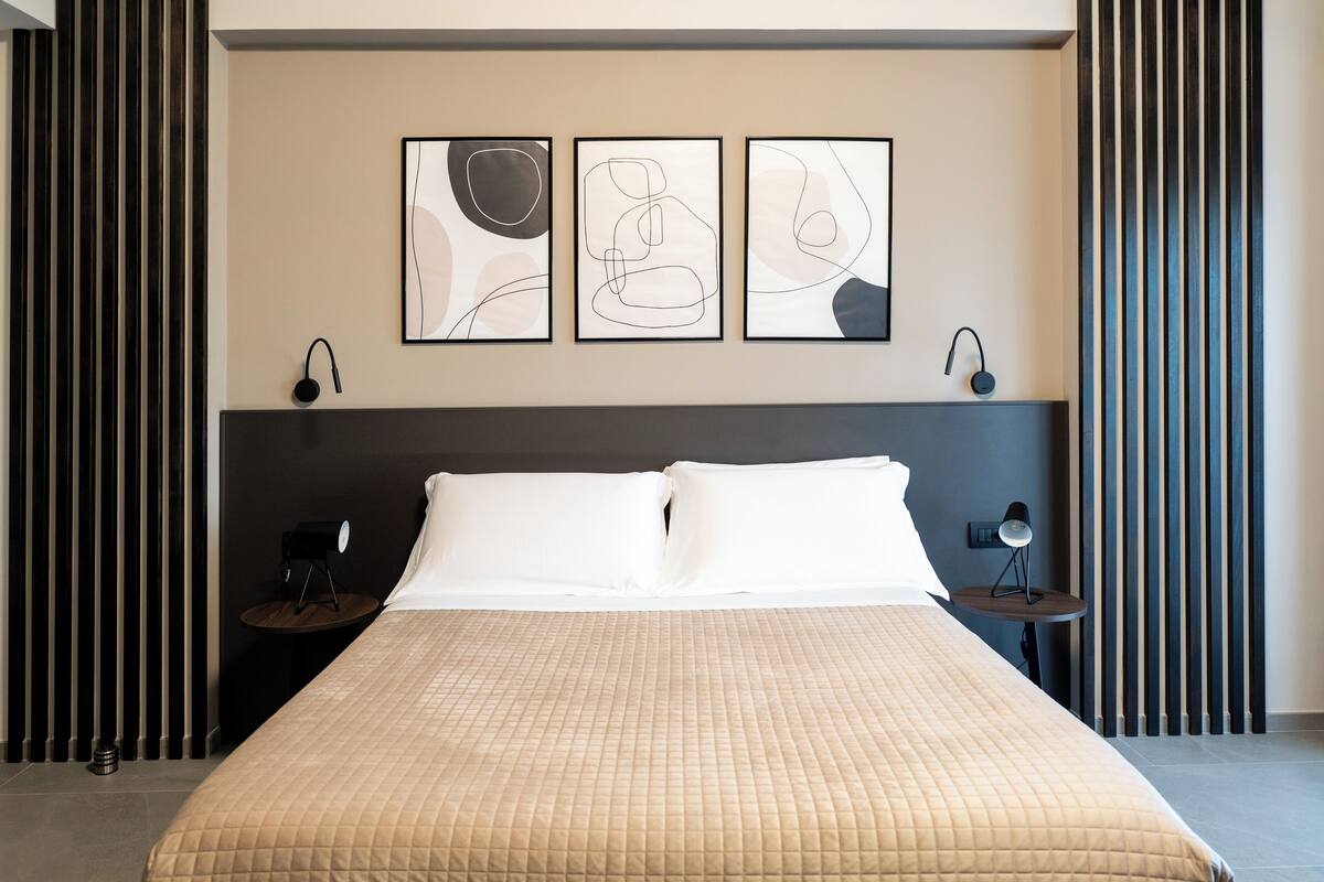 A modern bedroom with a large bed, a nightstand, a lamp, and abstract artwork on the wall.