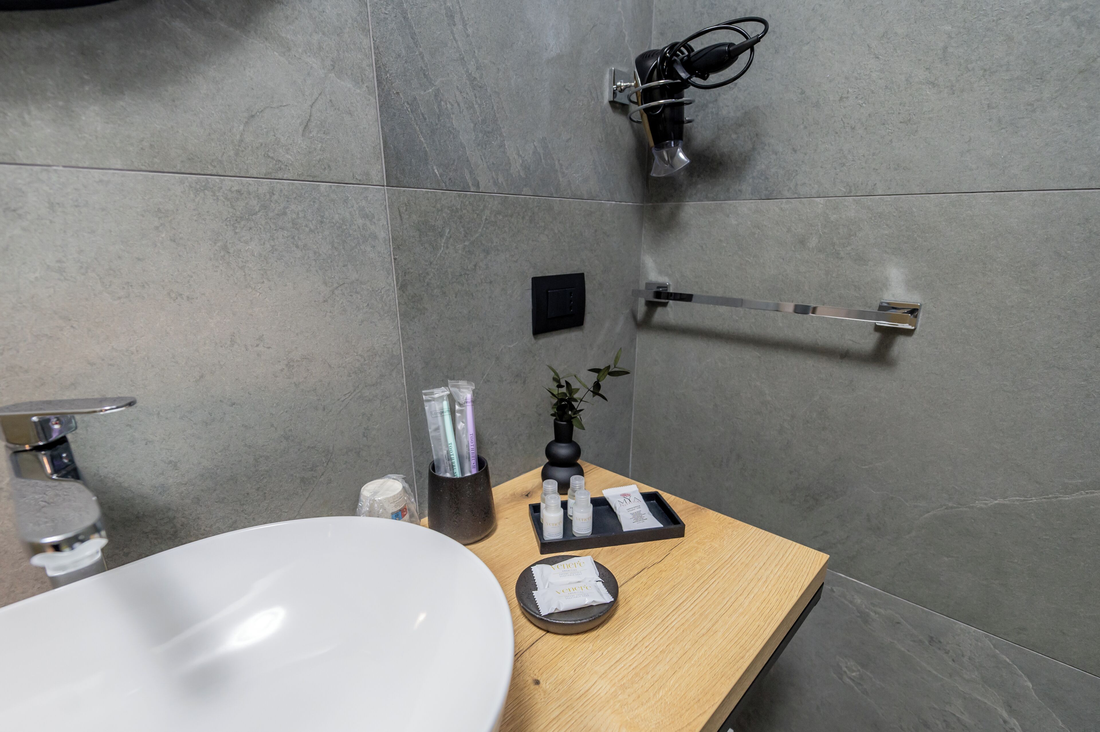Un baño moderno con un lavabo blanco, tocador de madera, toallero y dispensador de toallas.