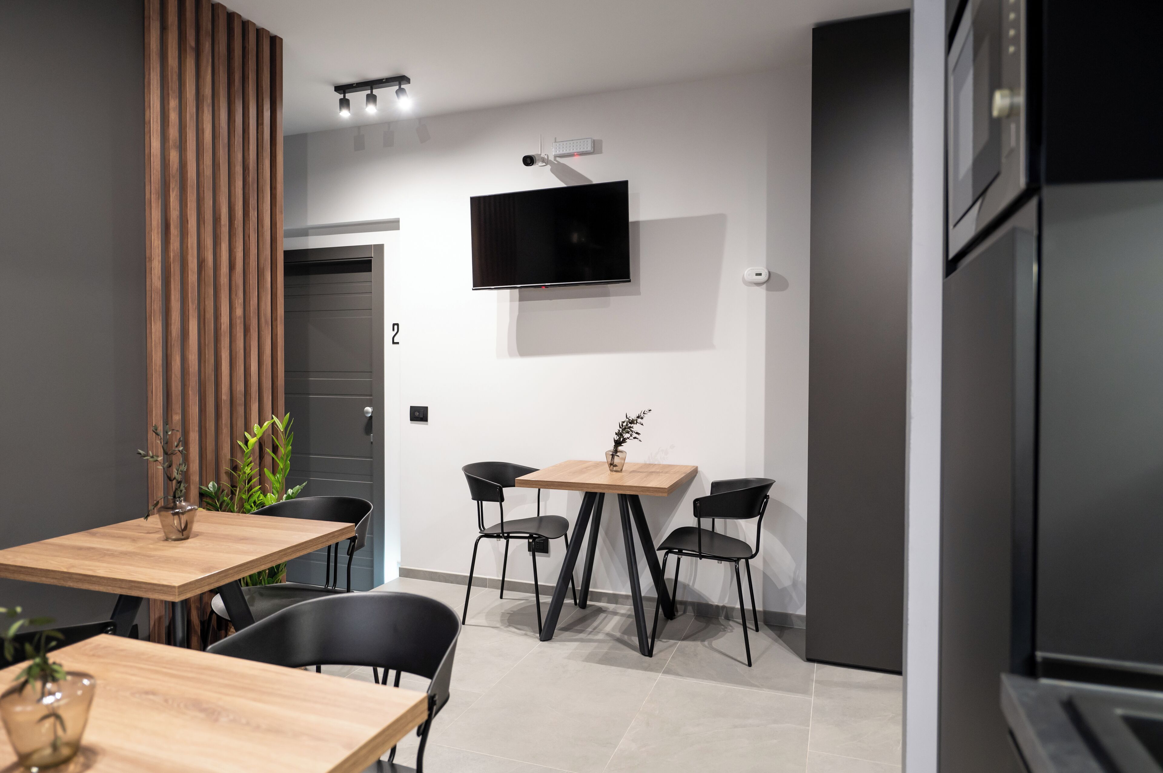 A modern kitchen with a built-in oven, a wooden dining table with four chairs, and a flat-screen TV mounted on the wall.