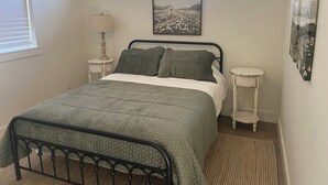 A bedroom with a bed, a nightstand, a lamp, a window, and a picture on the wall.