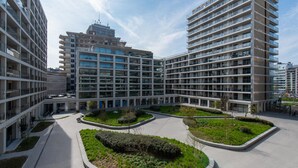 Un ensemble immobilier moderne composé de plusieurs étages, avec une cour intérieure agrémentée de verdure et un ciel dégagé.