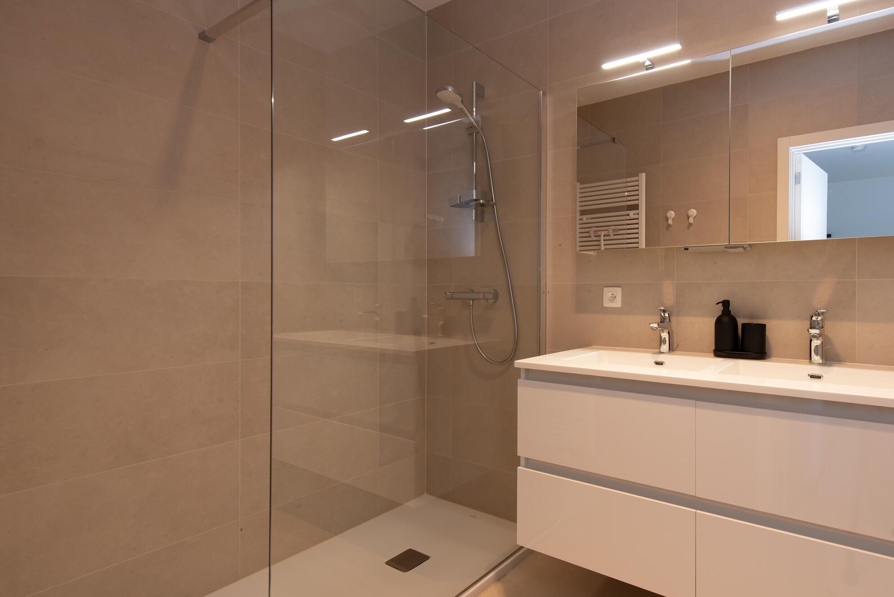 Casa de banho moderna com chuveiro em cabine de vidro, toucador branco com espelho e porta-toalhas.
