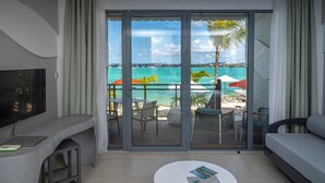 Une chambre d’hôtel moderne avec un balcon donnant sur une plage, une télévision à écran plat, un canapé et une table basse.