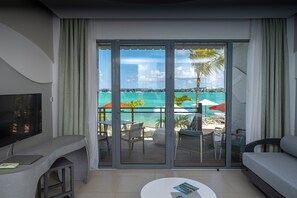 A modern hotel room with a balcony overlooking a beach, a flat-screen TV, a sofa, and a coffee table. - Baystone Boutique Hotel & Spa (Grand-Baie)