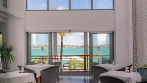 A modern dining area with tables and chairs, large windows with a view of the sea, and a ceiling with a unique light fixture. - Baystone Boutique Hotel & Spa (Grand-Baie)