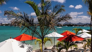 A beachside resort with sun loungers and umbrellas, a clear blue sky, and turquoise water. - Baystone Boutique Hotel & Spa (Grand-Baie)