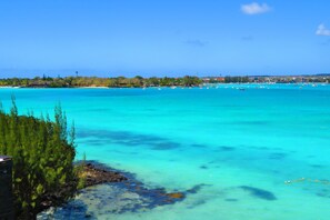 A coastal view with clear turquoise waters, a rocky shoreline, and a distant town with buildings and greenery. - Baystone Boutique Hotel & Spa (Grand-Baie)