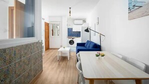 Ein modernes Wohnzimmer mit einem blauen Sofa, einem Esstisch und einer Küche im Hintergrund.