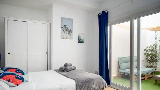 Ein Schlafzimmer mit Bett, Kleiderschrank und einem Fenster mit Blick auf eine Außenlounge.