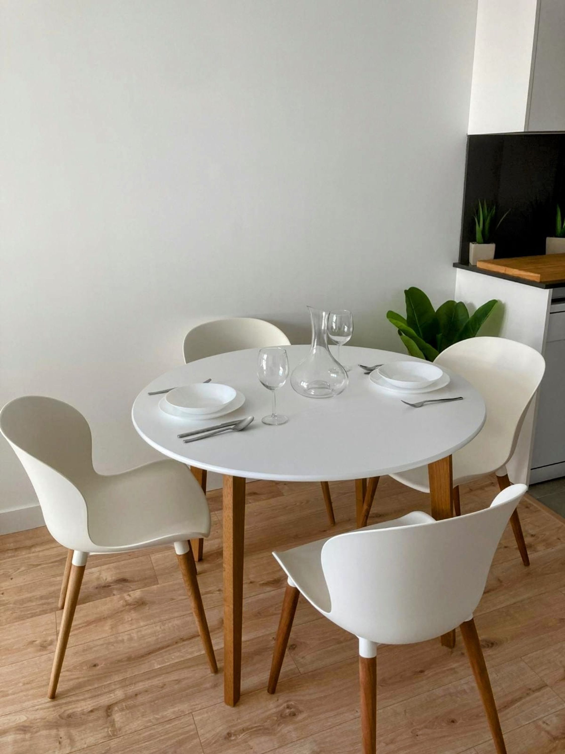 Una mesa redonda para comer con sillas blancas, un florero blanco y copas de vino.