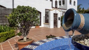 A courtyard with a fountain, a potted tree, and a building with arched windows. - Happy Travel La Maestranza 5A (Marbella)