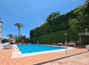 A swimming pool with tiled flooring, lounge chairs, and a hedge in the background. - Happy Travel La Maestranza 5A (Marbella)