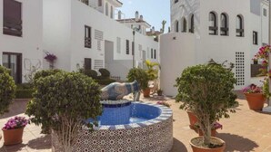 A courtyard with a fountain, potted plants, and a white building with arched windows. - Happy Travel La Maestranza 5A (Marbella)