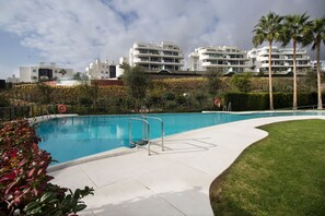 A swimming pool with a metal ladder, surrounded by a well-maintained lawn and palm trees. - Happy Travel Higueron West (Fuengirola)