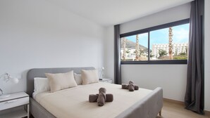 Ein modernes Hotelzimmer mit einem großen Bett, einem Nachttisch mit Lampe und einem Fenster mit Blick auf die Stadt.
