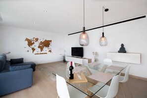 A modern living room with a glass dining table, white chairs, a grey sofa, a world map on the wall, a TV, and a statue on a shelf. - Happy Travel Higueron West (Fuengirola)