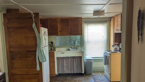 A compact kitchen with wooden cabinets, a refrigerator, a sink, and a window with blinds.