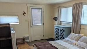 A bedroom with a bed, a dresser, a window with blinds, a door, and a ceiling light.