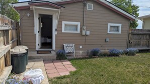 A single-story house with a front door open, a small porch, and a garden with blue flowers.