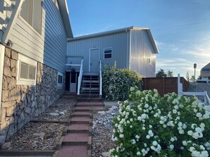 A house with a stone wall, a wooden staircase, and a white flowering bush.