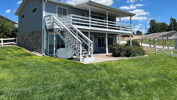 A two-story house with a covered porch and a staircase leading to the upper level. - Home Near Lake McConaughy (Lewellen)