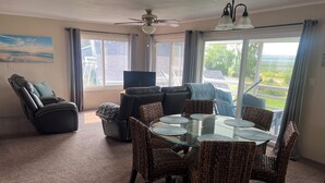 A living room with a glass-top dining table surrounded by wicker chairs, a black leather recliner, and a ceiling fan. - Home Near Lake McConaughy (Lewellen)
