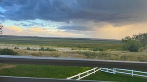 A view from a balcony overlooking a grassy field with a white fence and a cloudy sky. - Home Near Lake McConaughy (Lewellen)