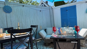 En uteplats med ett bord och stolar, en grill och en eldstad.