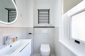 A modern bathroom with a white sink, a toilet, a towel rack, and a mirror. - YTD Residential (London)