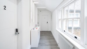 A bright hallway with white walls, a wooden floor, and a radiator. There are doors numbered 2 and 4, and a small table with cups and a phone on it. - YTD Residential (London)