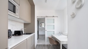 A compact kitchen with a microwave, toaster, and sink. There's a chair and a small table with glasses. - YTD Residential (London)