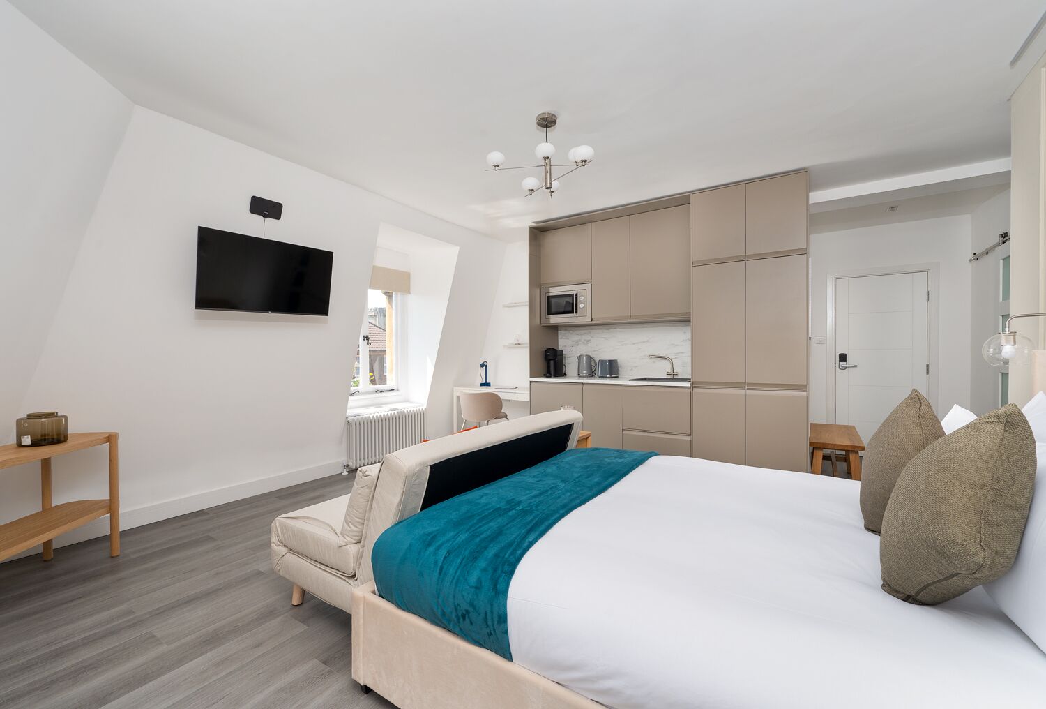 A modern bedroom with a bed, a desk, and a kitchenette.