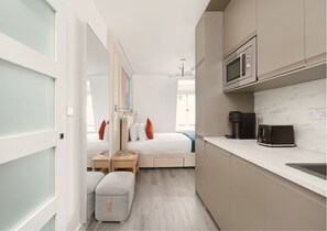 A compact hotel room with a bed, bedside table, and a kitchenette area including a microwave and coffee maker. - YTD Residential (London)