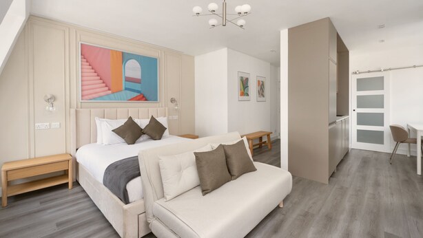 A modern bedroom with a large bed, a sofa, a desk, and a staircase. - YTD Residential (London)