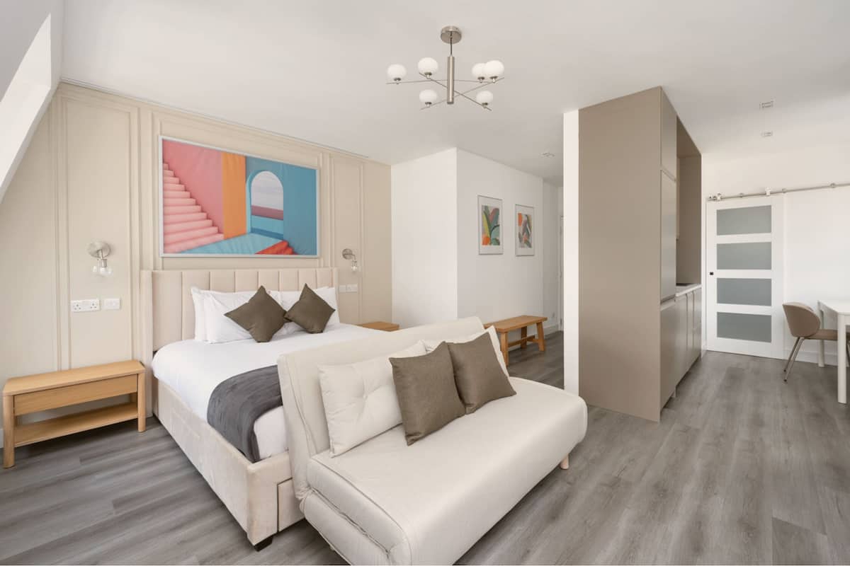 A modern bedroom with a large bed, a sofa, a desk, and a staircase.
