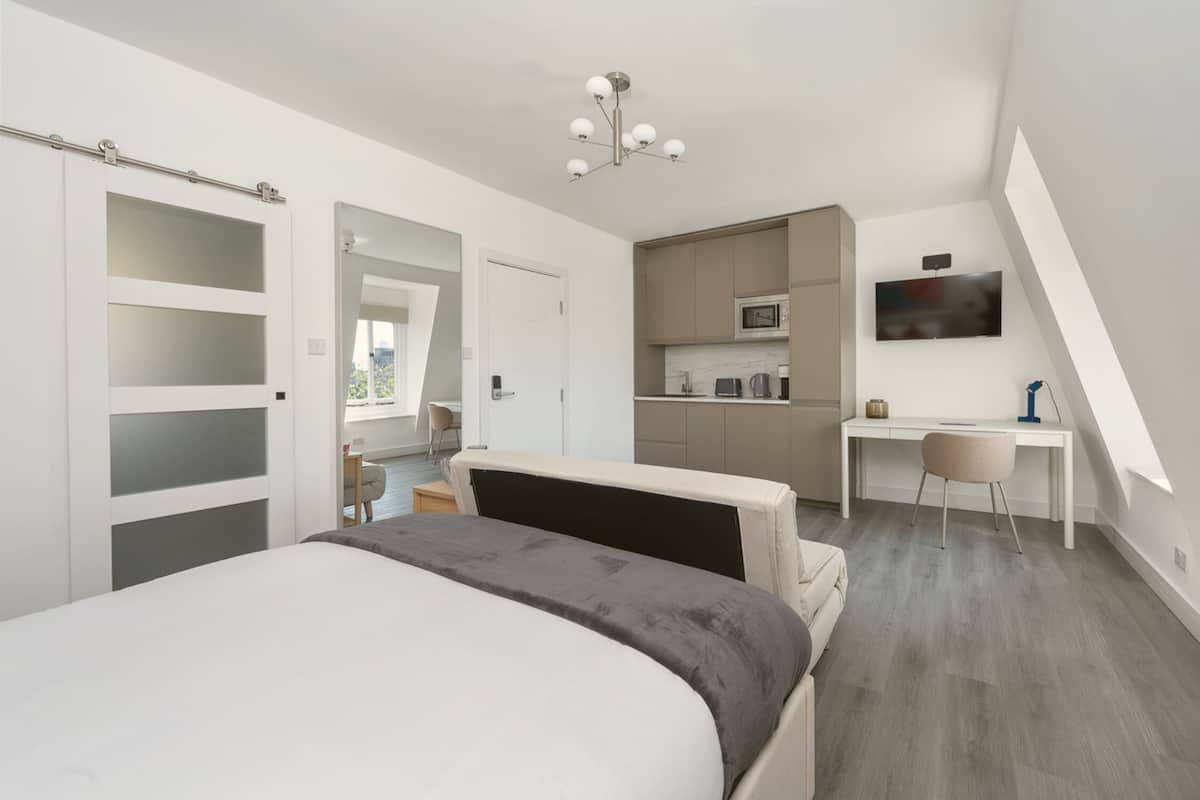 A modern bedroom with a large bed, a desk, and a kitchenette.
