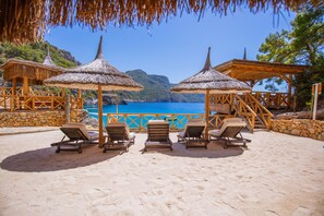 Ein Strand mit Reetsonnenstühlen, Liegestühlen und einer Steinmauer.