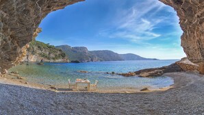 A rocky cave opening to a beach with clear water and a table with chairs. - Gökçe Villa (Fethiye)