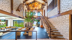 Un interior espacioso con pared de piedra, una escalera de madera y una amplia zona de estar con vistas al exterior.