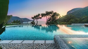 Una piscina con agua cristalina, rodeada de escalones de piedra y vistas a montañas y árboles.
