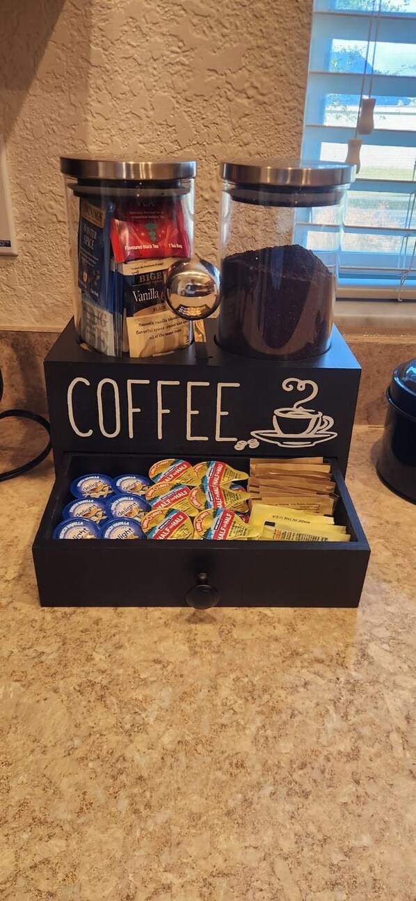 A coffee station with a grinder, a coffee maker, and a box labeled "COFFEE" containing coffee pods.