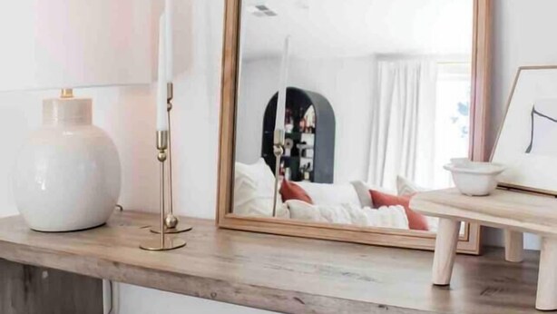 Une pièce avec un grand miroir, une lampe et une petite table sur laquelle est posé un cadre photo. On y trouve deux coins salon avec des fauteuils confortables.