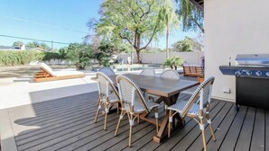 Une terrasse extérieure avec une plateforme en bois, une table à manger avec des chaises et un barbecue.