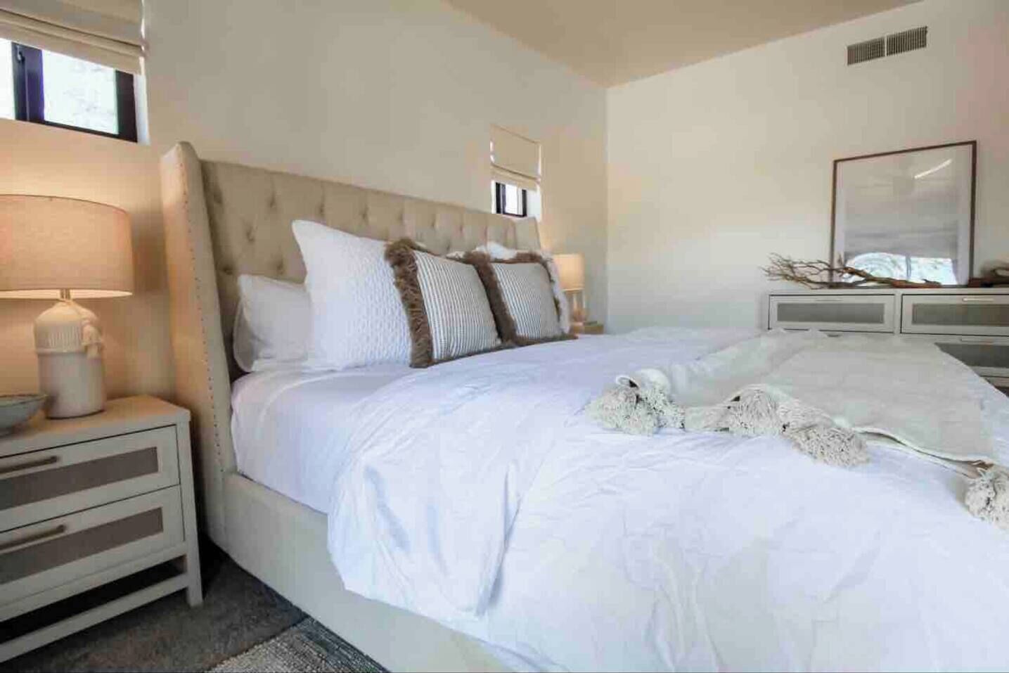 A bedroom with a large bed, a nightstand with a lamp, and a dresser.