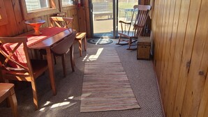 Een gezellig blokhut interieur met een houten eettafel, stoelen en een bankje. Er is een groot raam en een deur naar buiten.
